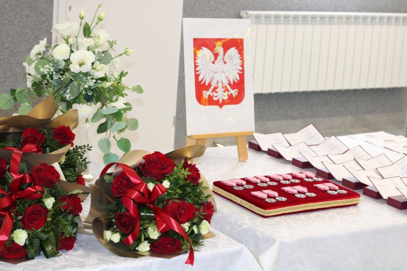 Zdjęcie przedstawiające leżące na stole medale, legitymacje, laurki oraz kwiaty